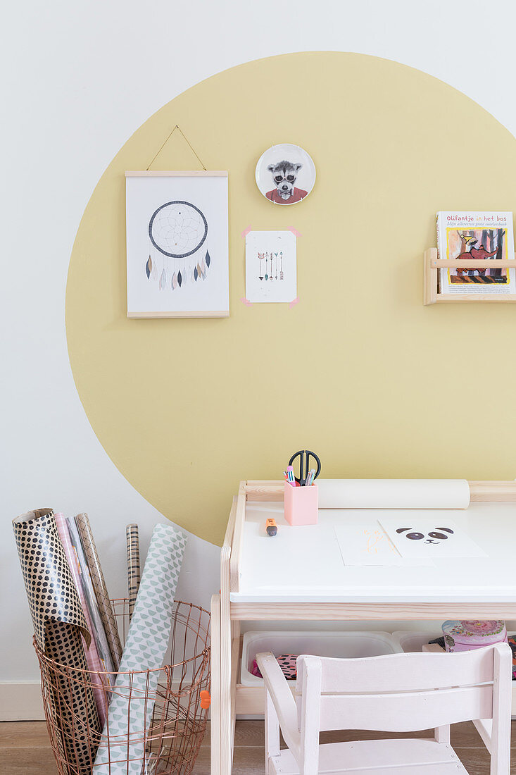 Schreibtisch und Korb mit Papierrollen vor Wand mit gelbem Punkt