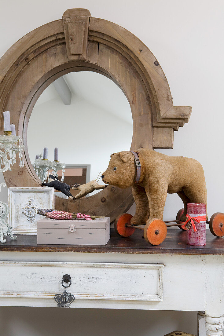 Old toy bear on wheels in front of oval mirror with wooden frame