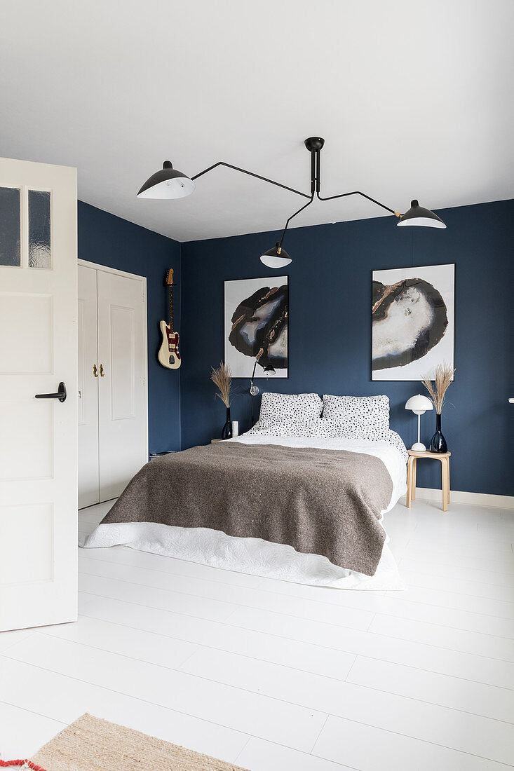 Doppelbett im Schlafzimmer mit blauer Tapete, großformatigen Kunstwerken und weißer Dielenboden