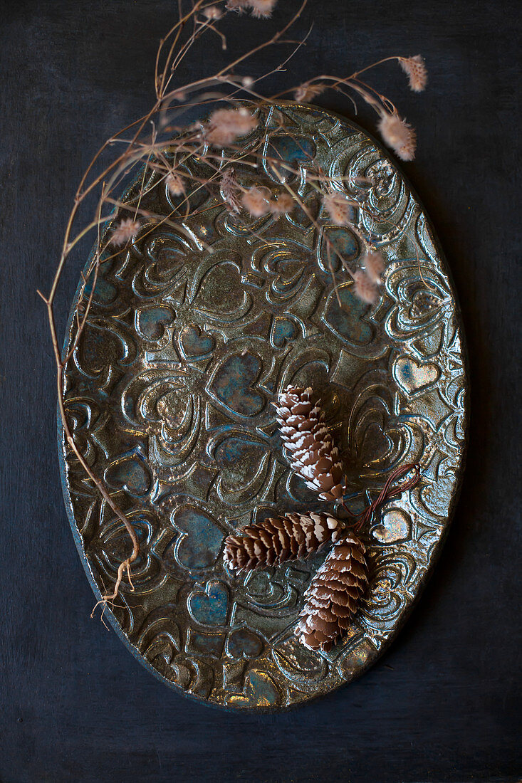 Three pine cones on oval plate with embossed love-heart pattern