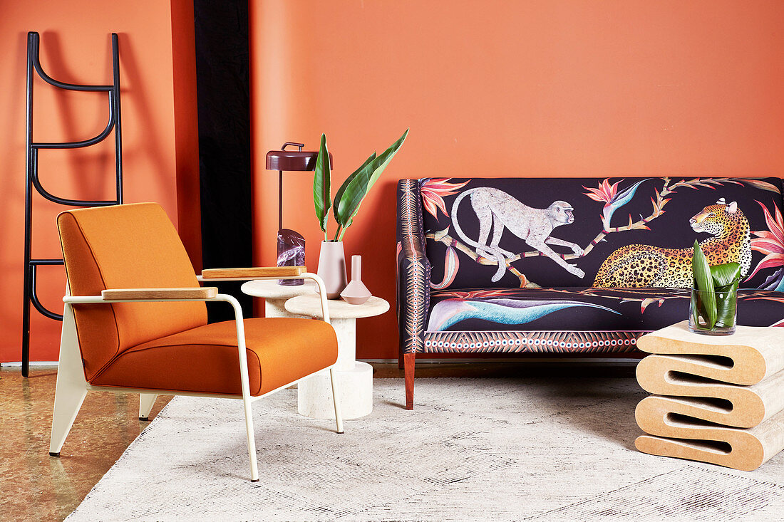 Designer sofa with animal-patterned upholstery, side table, ladder, armchair and coffee table in living room with orange wall