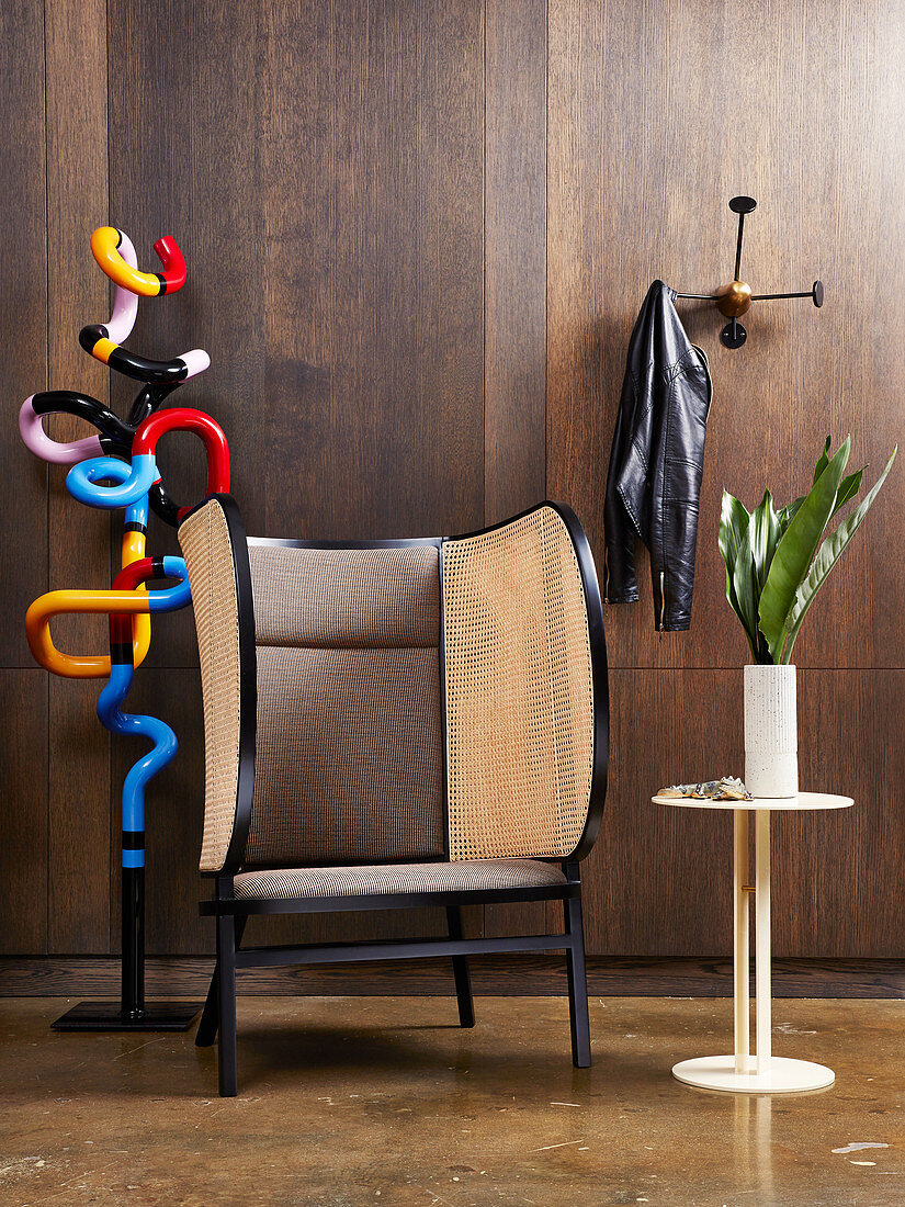 Colourful metal sculpture, designer wing-back chair and side table in front of wall with dark wooden panelling