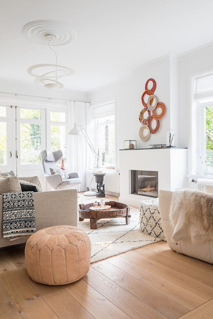 Pale seating, Moroccan pouffe, coffee table and fireplace in living room
