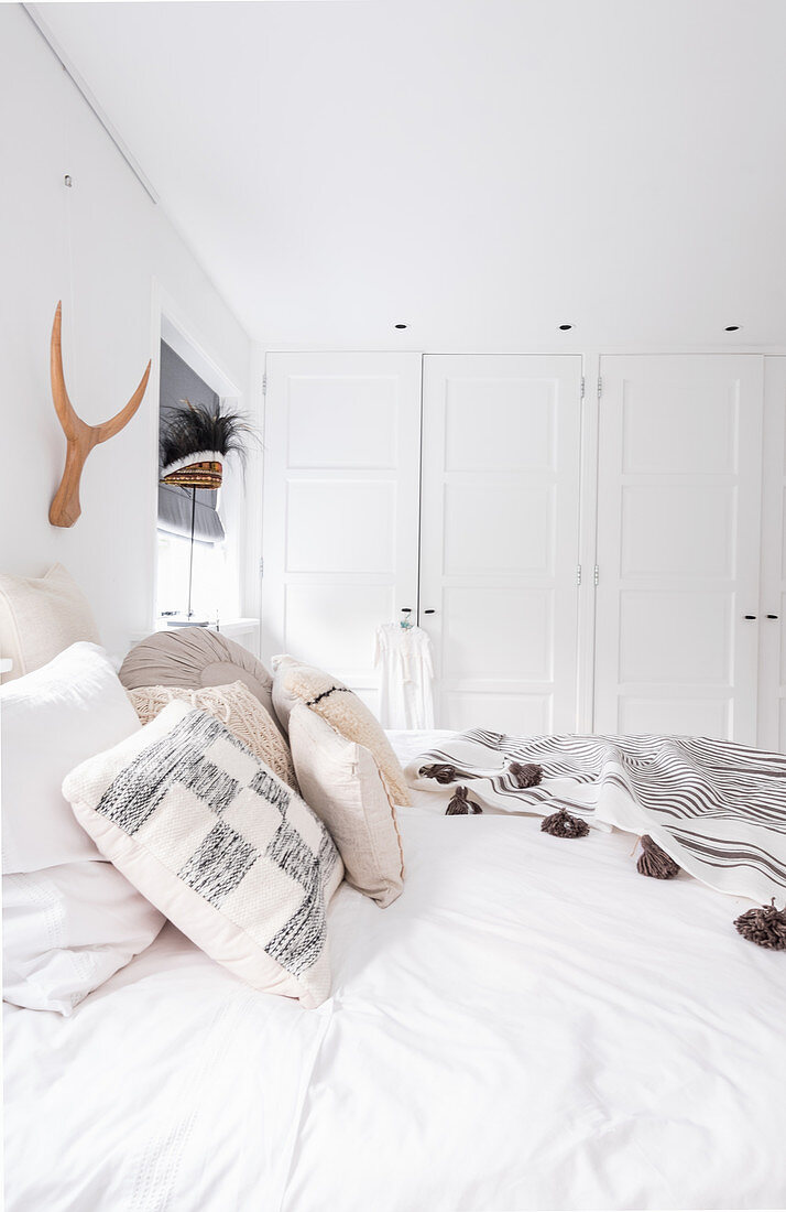 Blick über Doppelbett auf Einbauschränke in weißem Schlafzimmer