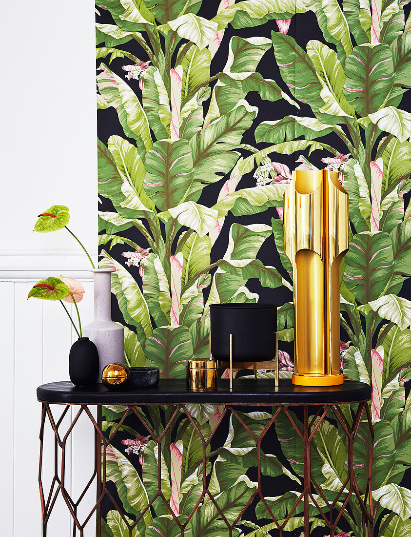 Black and gold ornaments on table against wall with leaf-patterned wallpaper
