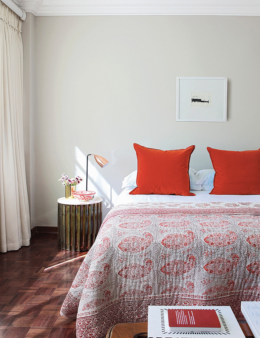 Red-patterned bedspread and red pillows on double bed in bright bedroom