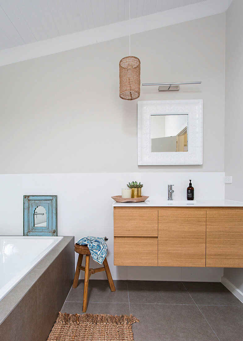 Waschtisch mit Holzfront, Holzhocker und Badewanne im Badezimmer mit hellgrauer Wand