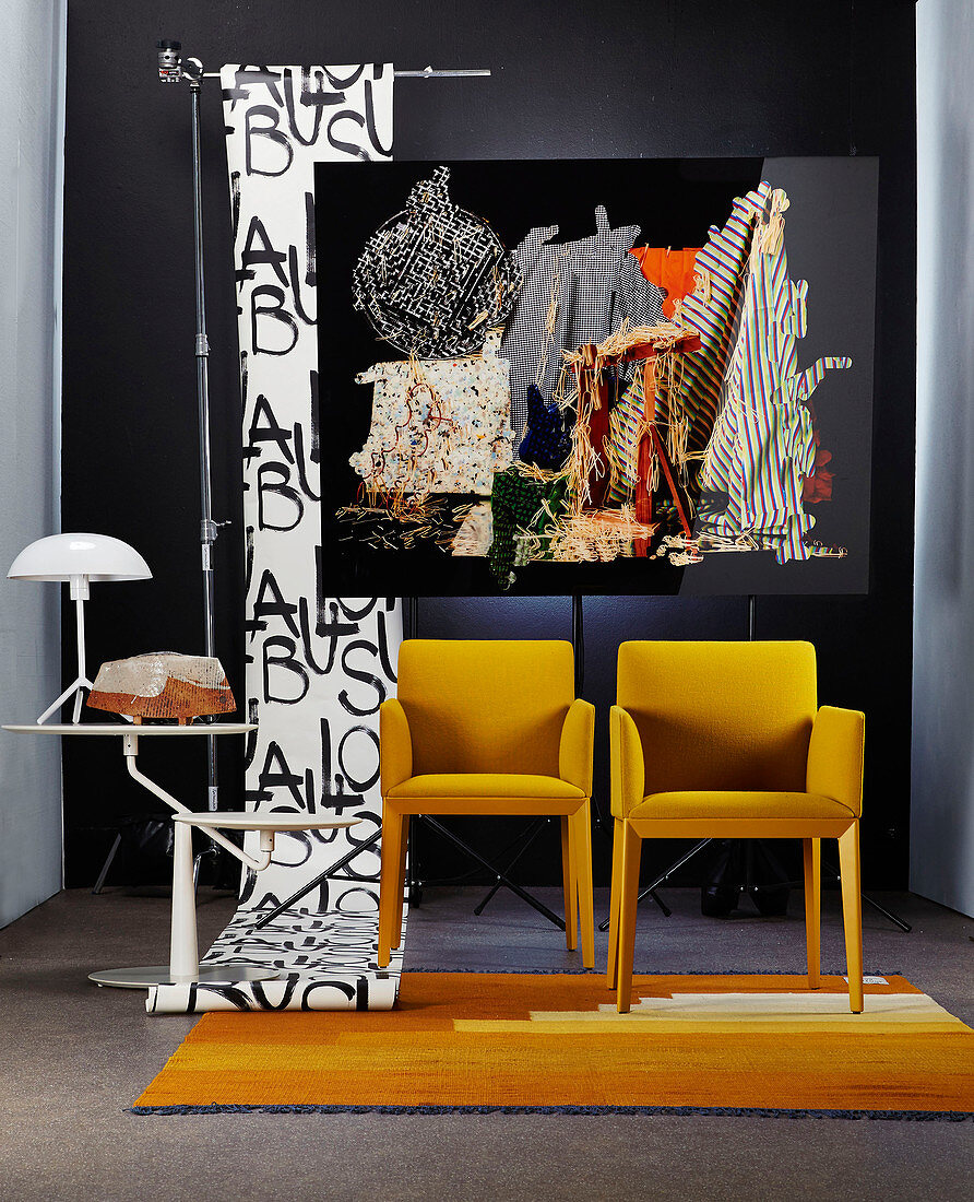 Yellow chairs and side table in front of photographic artwork and roll of wallpaper