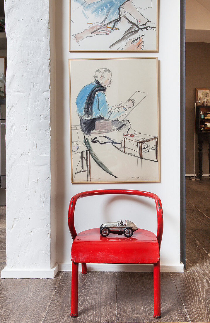 Red chair below paintings on wall