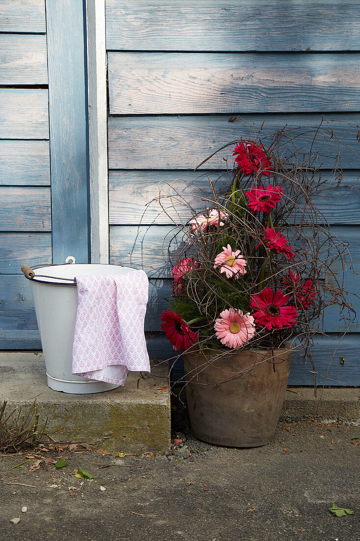 Arrangement of gerbera daisies next to bucket and cloth on stone step