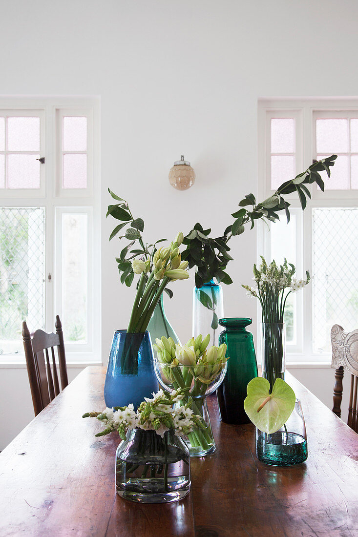 Glasvasen mit Blumen und Blätterzweigen auf rustikalem Esstisch