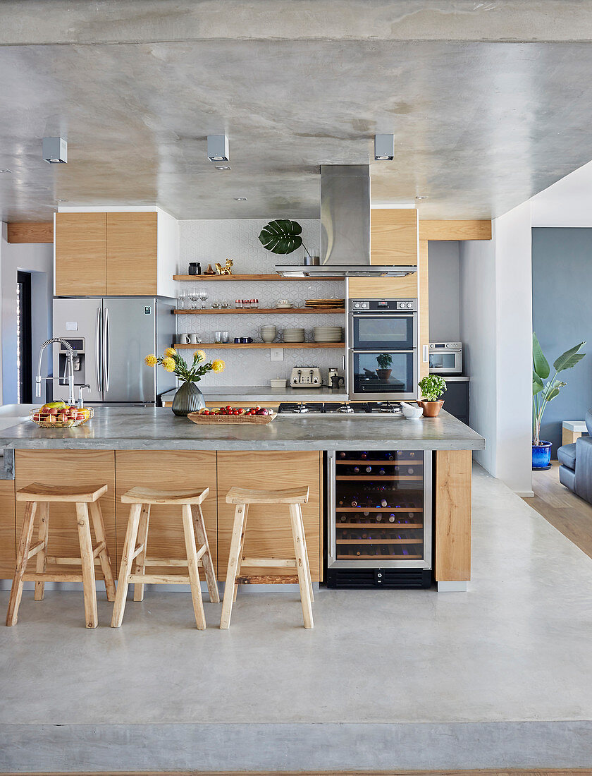 Island counter, bar stools and pale wooden fronts in open-plan kitchen on concrete platform