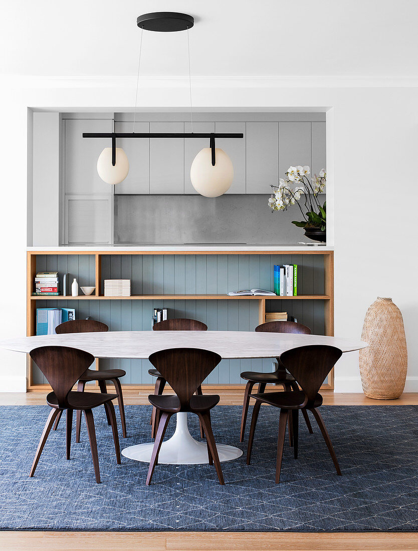 Oval dining table with designer chairs in front of an open shelf