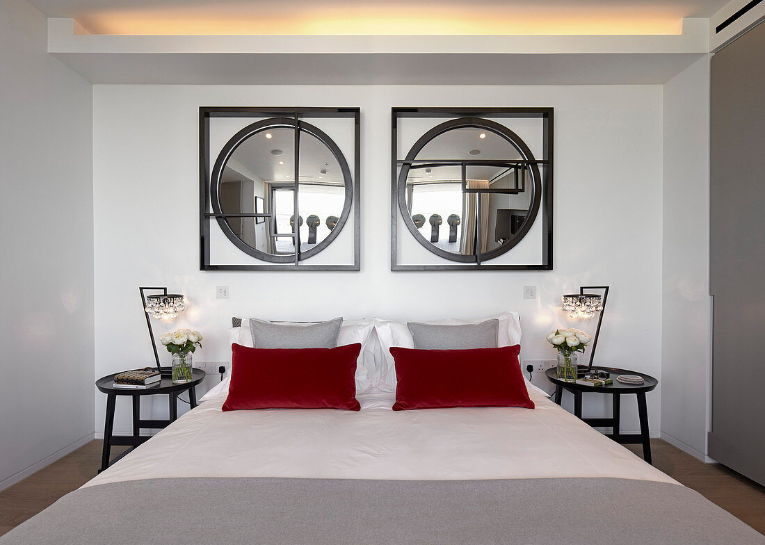 Two round mirrors in square frames above bed with red pillows