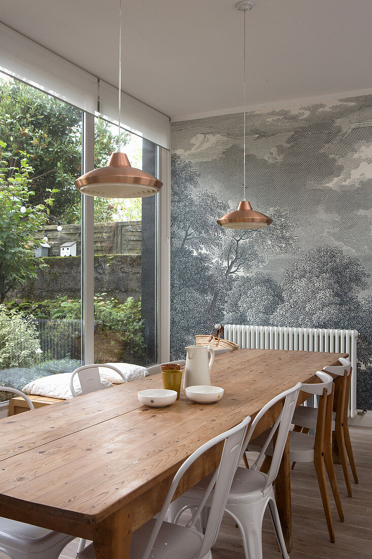 Long wooden table and chairs in front of mural wallpaper and next to terrace doors