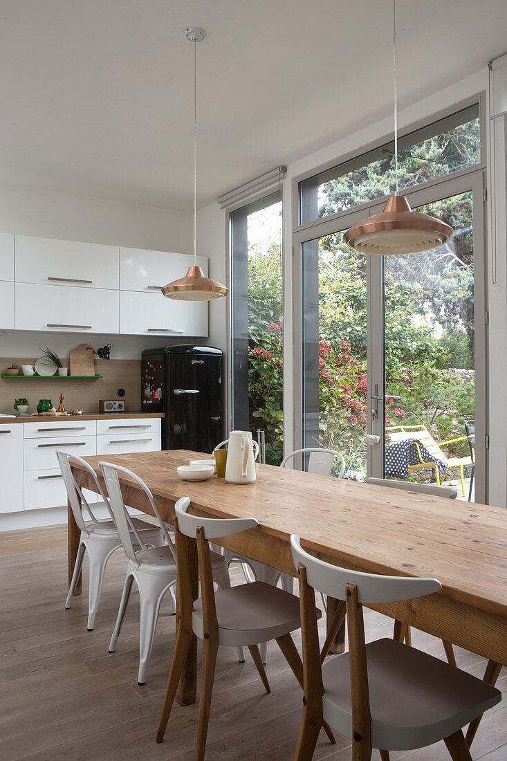 Langer Massivholztisch mit Stühlen vor Balkontür in offener, weißer Küche