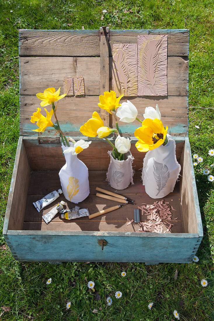 Alte Holzkiste mit Tulpen und Narzissen in Vasen mit Stoffbezug