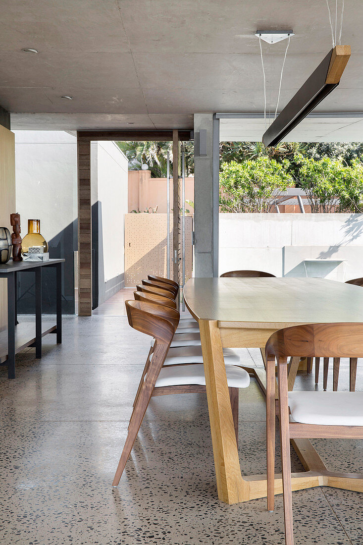 Modern wooden chairs at dining table in architect-designed house with concrete ceiling