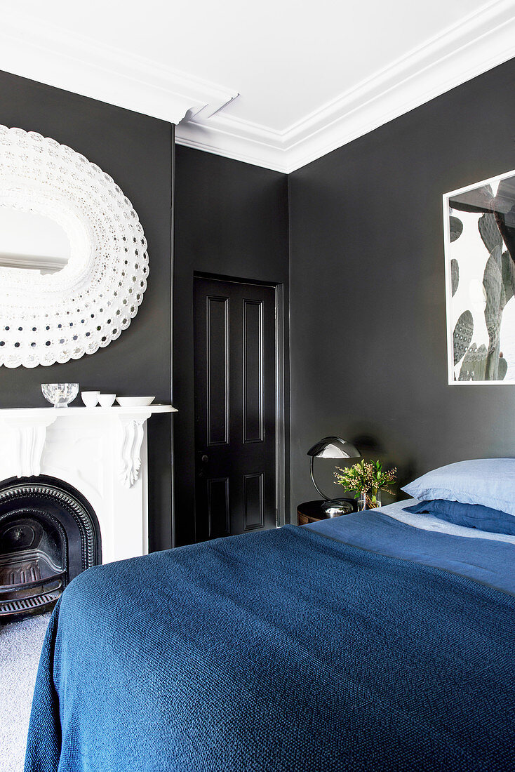 Double bed with dark blue bedspread, fireplace and mirror in the bedroom with black walls