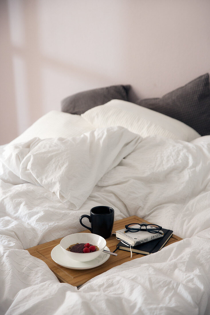 A book and glasses on a breakfast tray on a bed