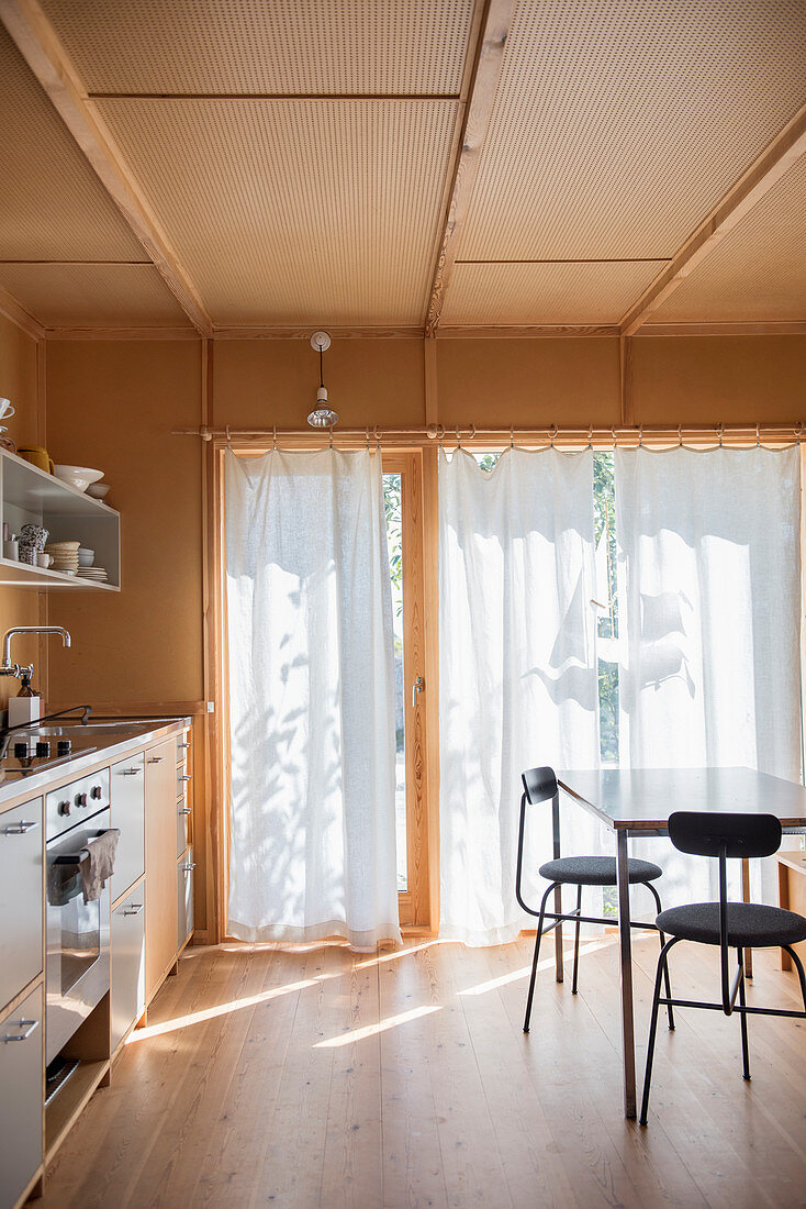 Küche mit Holzverkleidung und weißen Vorhängen an der Terrassentür