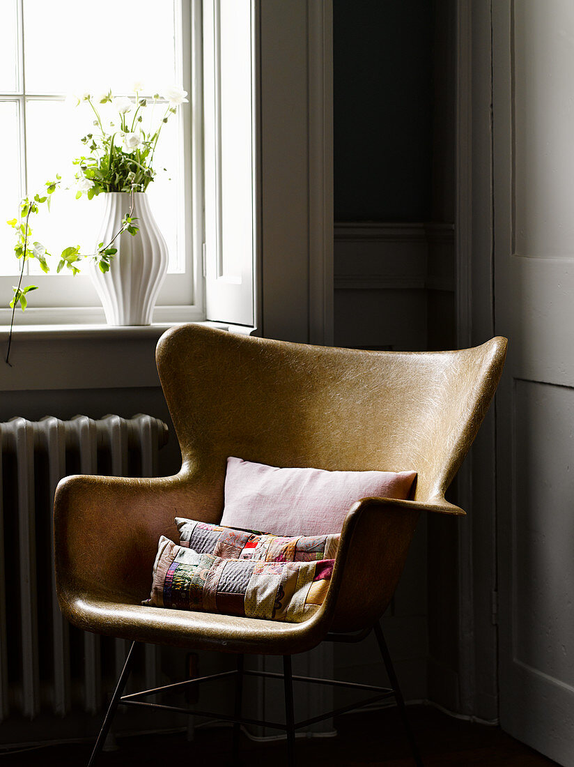 Colourful patchwork cushions on retro armchair below window