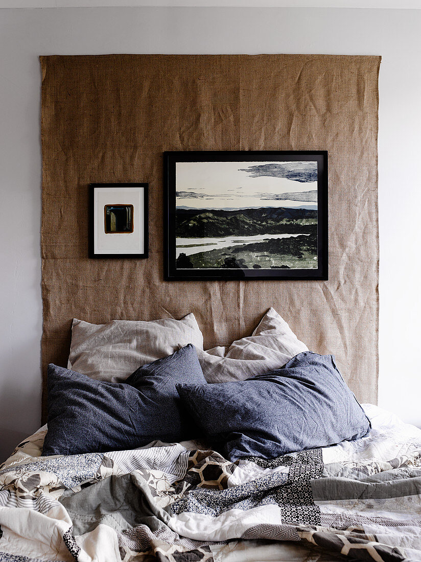 Wandbehang aus grobem Stoff über dem Bett mit Patchworkdecke
