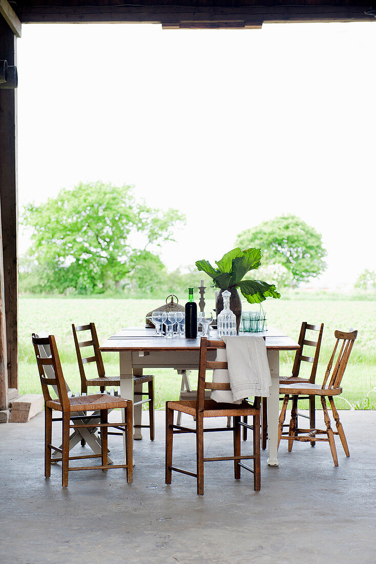Holzstühle um einen Tisch auf Betonboden mit Blick ins Grüne