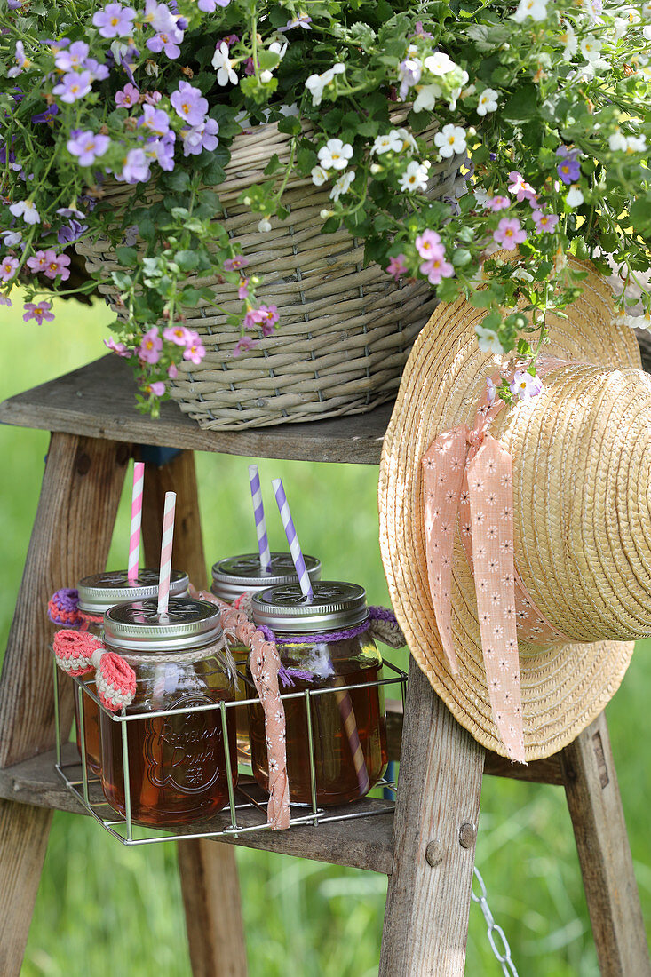 Schraubgläser mit Getränke, Blumen und ein Hut auf einer Leiter
