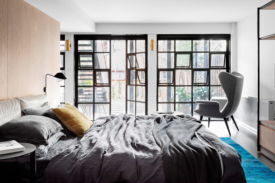 Doppelbett und Ohrensessel im Schlafzimmer mit Industriefenster und Terrassentür