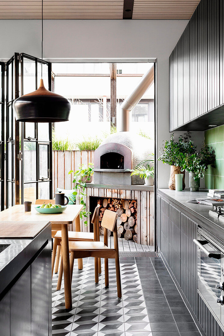 Schwarze Küchenzeile, Kücheninsel und Essbereich, im Hintergrund Pizzaofen auf der Terrasse