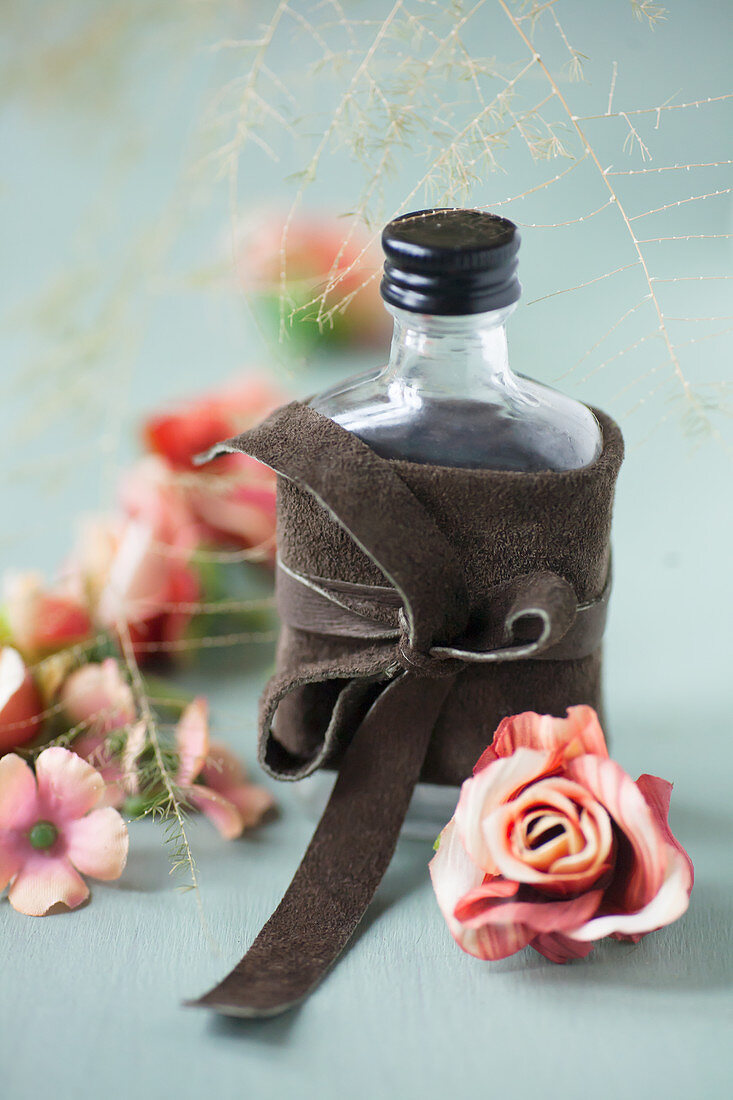 Fabric roses and bottle tied with leather bow on grey surface