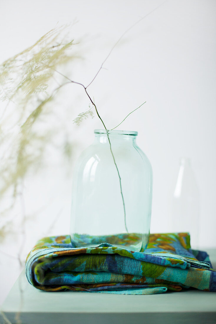 Zweig in einer Glasflasche auf blau-grünem, gefalteten Tuch