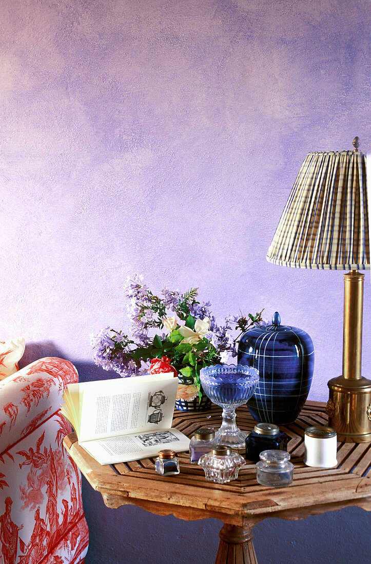 Döschen, Buch und Blumen auf dem Tisch vor lilafarbener Wand