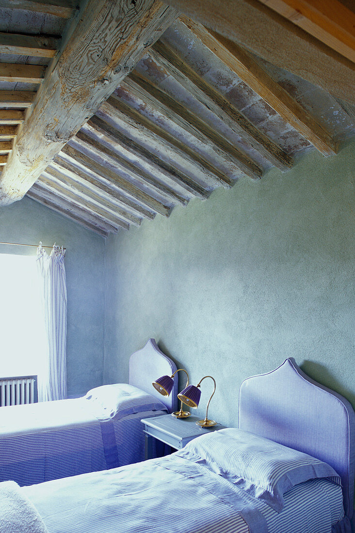 Zwei Einzelbetten mit lilafarbenem Betthaupt unter der Balkendecke