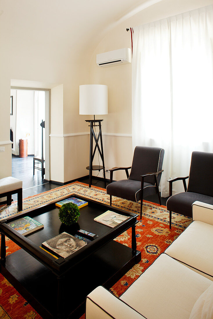Black rectangular coffee table, black armchairs, pale sofa and standard lamp in elegant lounge
