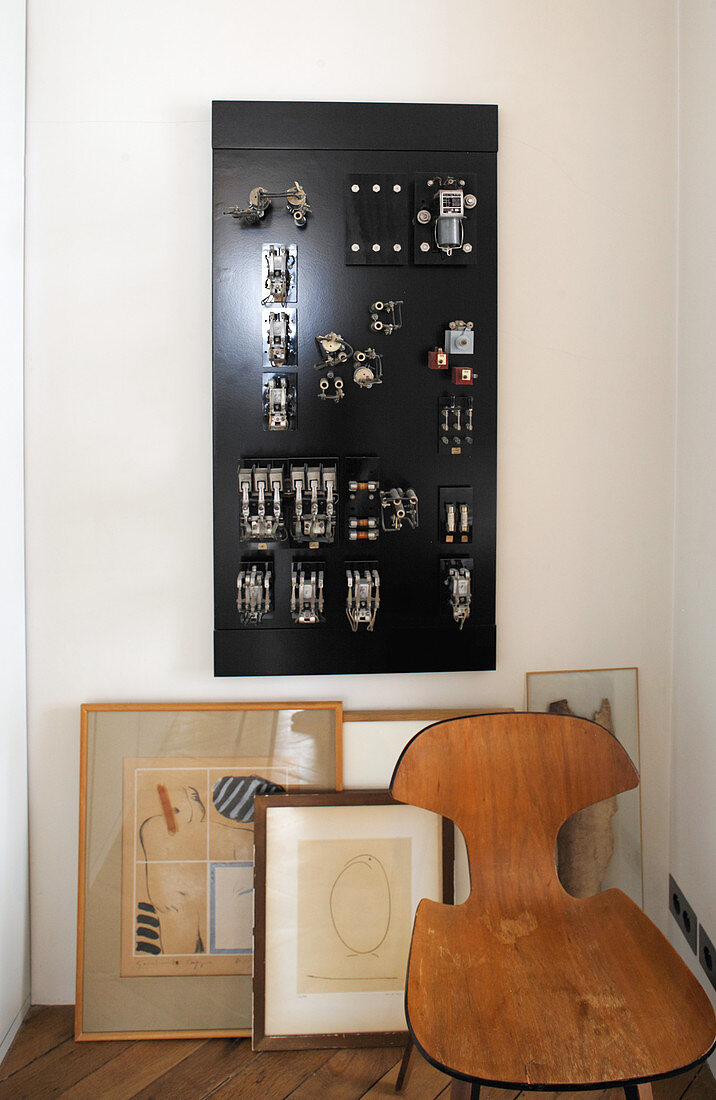 Wooden chair, pictures leaning against wall and electrical switchboard on wall