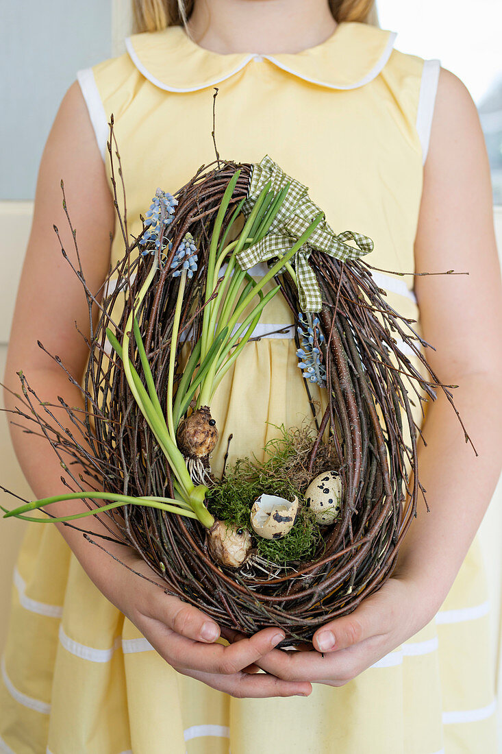 Mädchen hält Ei-förmigen Kranz aus Zweigen mit Blumen und Eierschalen
