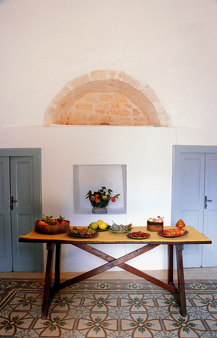 Rustikaler Holztisch mit Obsttellern auf mediterranem Musterfliesenboden