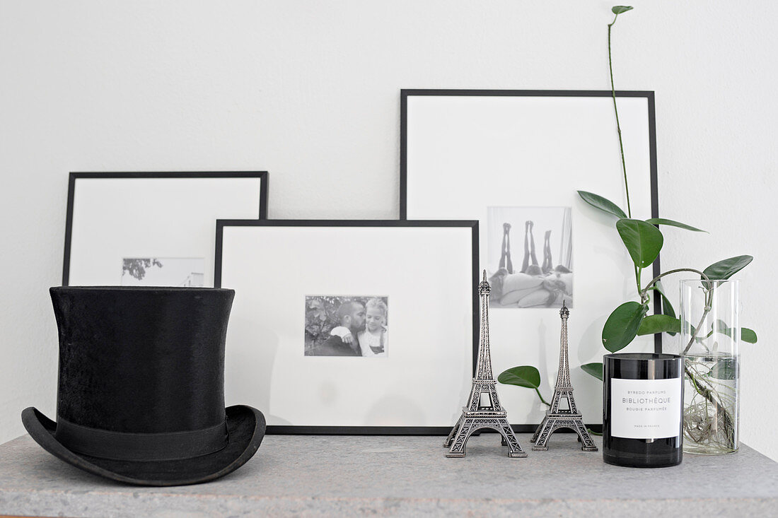 Grünpflanze, Eiffelturm-Miniature, eingerahmte schwarz-weiße Fotos und Zylinder auf Ablage