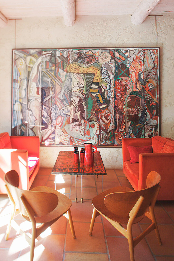 Mediterrane Lounge mit Holzstühlen, roter Sofagarnitur und großformatigem Kunstwerk an der Wand