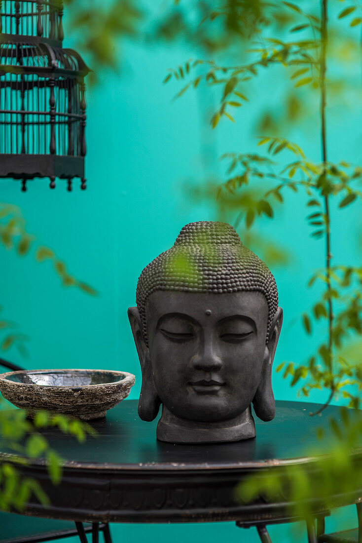 Buddhakopf auf schwarzem Tisch und Blätterranken vor türkiser Wand