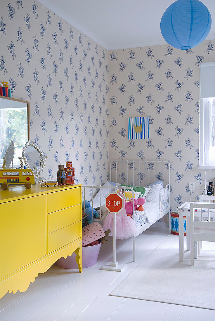 Yellow sideboard and metal bed in child's bedroom with blue and white wallpaper