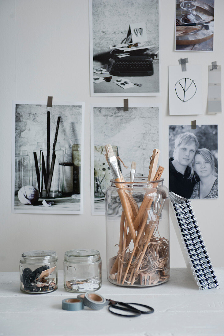 Gläser mit Büroutensilien vor einer Wand mit Schwarz-Weiß-Fotos