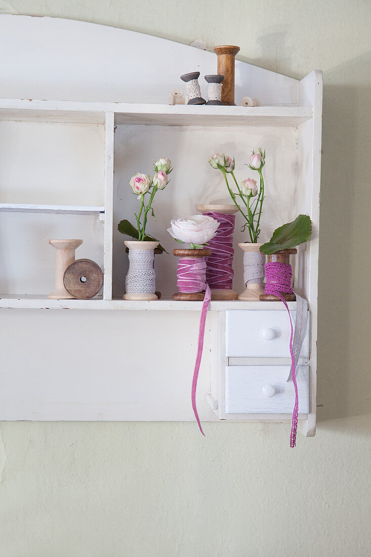 Flowers in yarn reels wound with ribbons on wall-mounted shelf