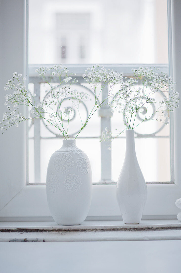 weiße Blumenvasen mit Schleierkraut auf Fensterbank