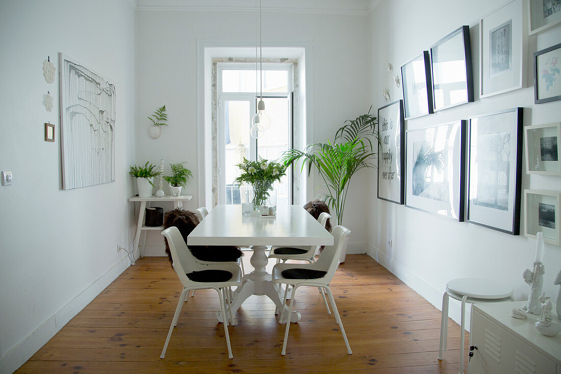 Weißes Esszimmer mit Grünpflanzen und mit Bildersammlung an der Wand