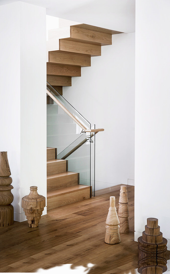 Elegantes Treppenhaus mit Holztreppe und Glasbalustrade, Holzskulpturen auf dem Boden