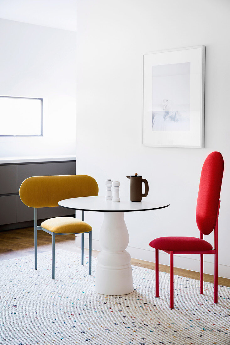 Runder Tisch und Designerstühle vor weißer Wand