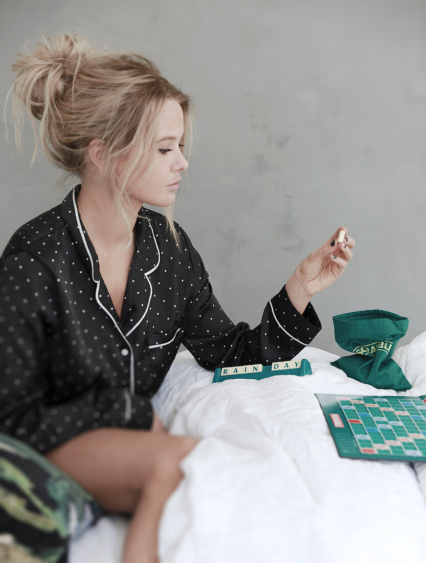 Junge Frau im Pyjama spielt Scrabble im Bett